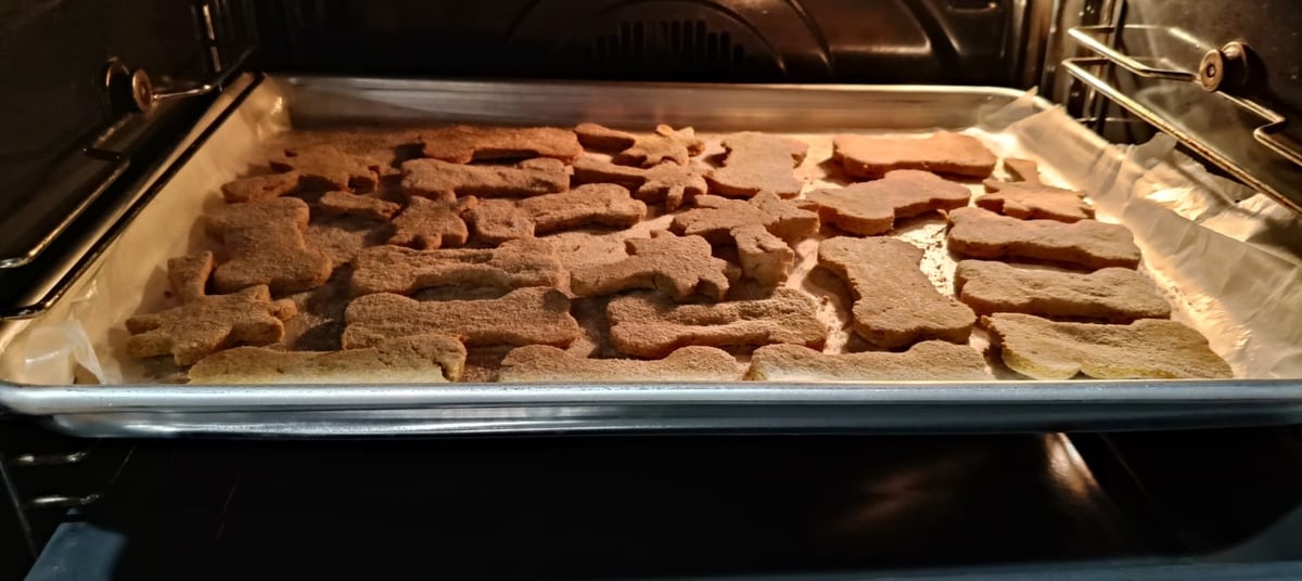 Galletas para perros caseras en forma de hueso horneándose en el horno sobre una bandeja metálica